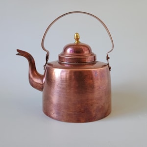 Peut inclure: Une bouilloire à thé en cuivre poli avec un bec verseur incurvé, un couvercle arrondi surmonté d'un petit bouton de couleur laiton et une anse arquée. Le corps de la bouilloire présente une finition brun-rouge métallique et chaude.