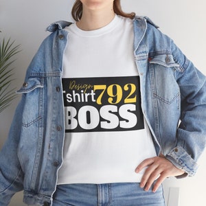 Puede incluir: Camiseta blanca con texto negro que dice "Design tshirt 792 BOSS". El texto está en fuente amarilla. La persona lleva una chaqueta vaquera azul.