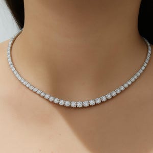 Puede incluir: Un delicado collar con una serie de gemas redondas y brillantes. El collar está engarzado en un metal plateado o blanco y descansa elegantemente sobre el escote. Las gemas están espaciadas uniformemente, creando una línea continua de brillo.