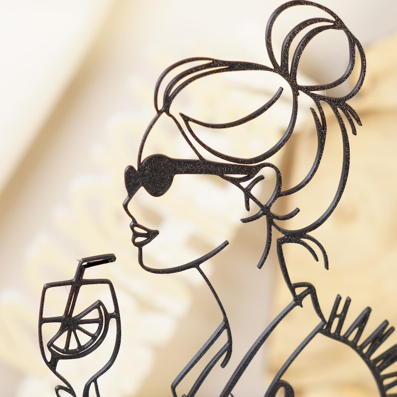 以下が含まれることがあります： サングラスをかけた女性がストローで飲み物を飲んでいる黒い金属製のシルエット。女性の髪はまとめられています。飲み物には柑橘系の果物のスライスが見えます。「HAMM」という言葉が部分的に見えます。