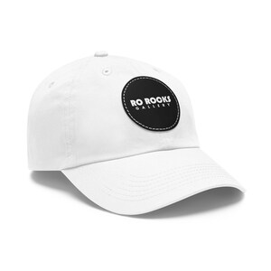 Könnte beinhalten: Weiße Baseballkappe mit einem schwarzen runden Patch, auf dem "RO ROCKS GALLERY" in weißer Schrift steht.