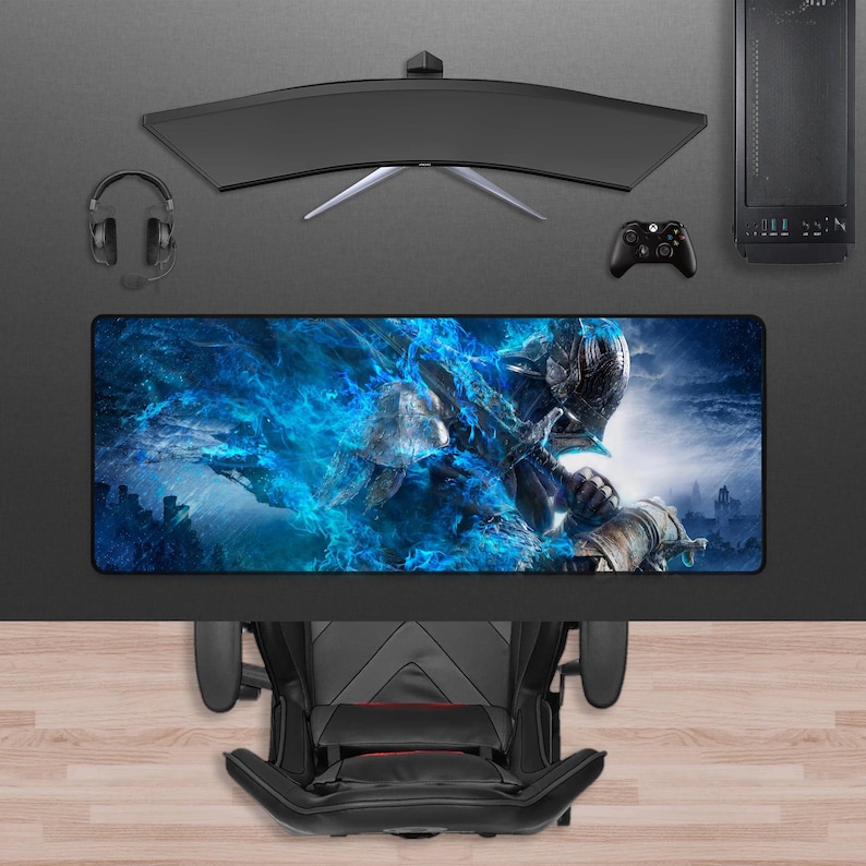 May include: A gaming setup featuring a curved monitor, headset, and a desktop computer. A large rectangular mousepad displays a fantasy warrior design with blue and white hues. A black gaming chair is positioned below the desk.