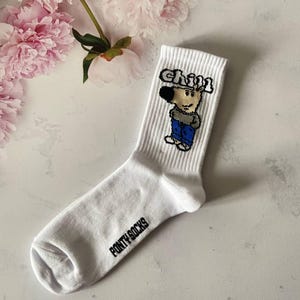 May include: White crew socks with a cartoon character wearing a hat and the word "chill" printed on the sock. The brand name "Fonty Socks" is printed on the bottom of the sock.