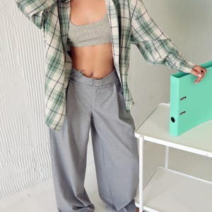 May include: A light gray bra, gray wide-leg pants, and a green and white plaid shirt. A mint green binder sits on a white rolling cart. The outfit is casual and stylish.