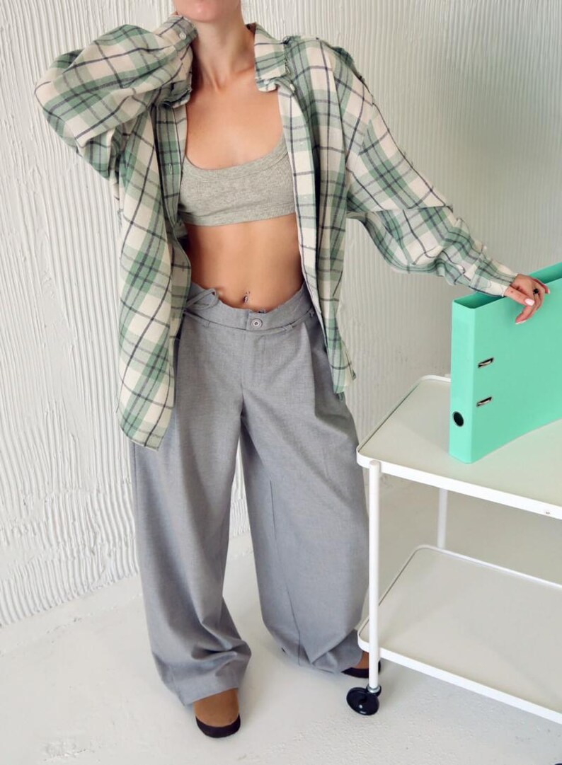 May include: A light gray bra, gray wide-leg pants, and a green and white plaid shirt. A mint green binder sits on a white rolling cart. The outfit is casual and stylish.