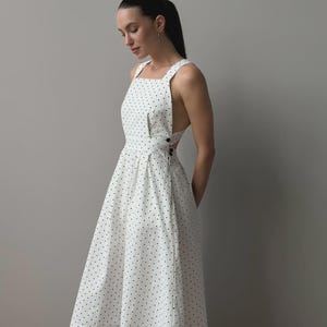 Puede incluir: Vestido blanco con lunares negros. El vestido sin mangas tiene un escote cuadrado y una falda acampanada. Cuenta con detalles de botones en el lateral. La tela est&aacute; estampada con peque&ntilde;os lunares negros espaciados uniformemente.