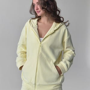 May include: A pale yellow zip-up hoodie and matching shorts. The hoodie features a drawstring hood, front pockets, and a full-length zip. The shorts have a drawstring waist. The outfit is made of a soft, comfortable material.