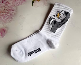 May include: White socks with a cartoon cat design, lounging in a chair and holding a snack. The socks have the text "PONY SOCKS" in black. The background includes pink peonies.