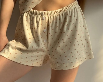 May include: A pair of cream-colored shorts with a small floral pattern. The shorts have a button fly and a wide elastic waistband.