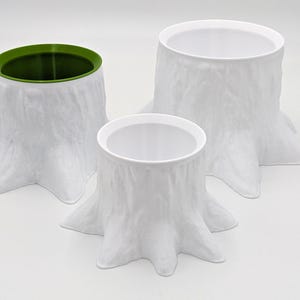 May include: Three white ceramic tree stump planters, one with a green rim. The planters are all different sizes and have a textured surface that resembles tree bark.