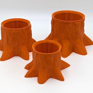 May include: Three orange ceramic tree stump planters of varying sizes. The planters are shaped like tree stumps with a hollow centre for planting.