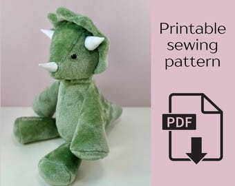 May include: A soft, green triceratops dinosaur toy with white horns and a friendly expression. The image includes the text "Printable sewing pattern" and a PDF icon, suggesting a sewing pattern for the toy.