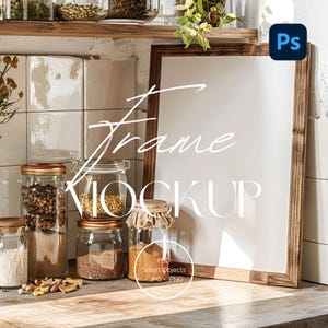 May include: A wooden framed mockup with the text "Frame Mockup" in white script. Several glass jars with gold lids and various contents are arranged on a wooden surface. The background includes white tiles and a shelf with more jars.