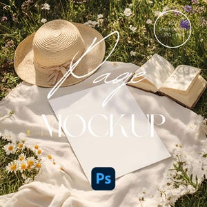 May include: A white sheet of paper with the text "Page Mockup" on it, lying on a white blanket with a straw hat and a book on it. The blanket is on a bed of green grass with white flowers.