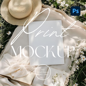 May include: A flat lay featuring a blank white print mockup with the text "Print Mockup" overlaid. A straw hat, open book, and flowers are arranged around the mockup on a cream-colored blanket. The image includes the Adobe Photoshop logo and text indicating PSD Smart Objects, JPG, and PNG formats.