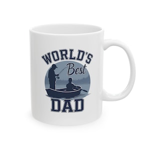 Könnte beinhalten: Weiße Keramiktasse mit einer blauen Grafik eines Vaters und Kindes beim Angeln in einem Boot. Der Text "WORLD'S Best DAD" ist oberhalb und unterhalb des Bildes in dunkelblauer, fetter Schrift gedruckt. Die Tasse hat einen gebogenen Griff.