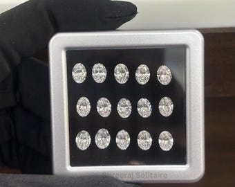 May include: A display case with a black interior holds twelve oval-cut diamonds. The diamonds are arranged in three rows of four, each sparkling with facets. The case is held by a gloved hand, with the text "Shreeraj Solitaire" visible.