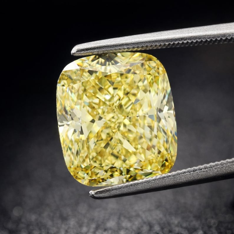 May include: A cushion-cut, fancy yellow diamond held by tweezers against a black background. The diamond's facets reflect light, creating a brilliant sparkle. The shape is square with rounded corners, showcasing its unique cut.