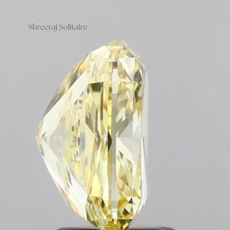 May include: A radiant, yellow-hued diamond with a unique cut. The gemstone is faceted, reflecting light and showcasing its clarity. The text "Shreeraj Solitaire" is visible in the upper left corner. The diamond's shape is elongated, with a pointed tip.