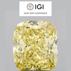 May include: A large, cushion-cut, yellow diamond with a brilliant, faceted surface. The diamond is set against a light gray background. The text "IGI SHOP WITH CONFIDENCE" is at the top.