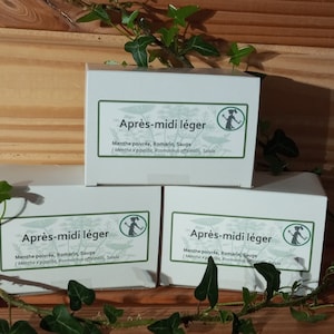 Peut inclure: Trois boîtes blanches avec le texte "Après-midi léger" et les mots "Menthe poivrée, Romarin, Sauge (Mentha x pipente, Rosmarinus offenali, Salvia" imprimés dessus. Les boîtes sont posées sur une surface en bois avec des feuilles vertes.