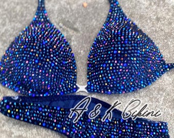 May include: A navy blue bikini with a halter top and a high-cut bottom. Both pieces are covered in iridescent rhinestones. The bikini is labeled "A&K Bikini".