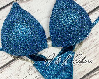 May include: A blue bikini with crystal embellishments. The bikini top has a halter style and the bottom is a high-cut style.