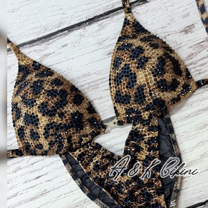 Peut inclure: Un bikini à imprimé léopard noir et marron avec des strass. Le haut du bikini est de forme triangulaire et le bas est de style taille haute. Le bikini est fait d'un tissu extensible et a un panneau en maille transparente sur le bas.
