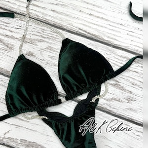 Könnte beinhalten: Ein dunkelgrüner Samt-Bikini mit einem mit Kristallen besetzten Band. Das Bikinioberteil hat eine Dreiecksform und das Unterteil ist ein frecher Schnitt. Der Bikini ist mit "A&K Bikini" gekennzeichnet.