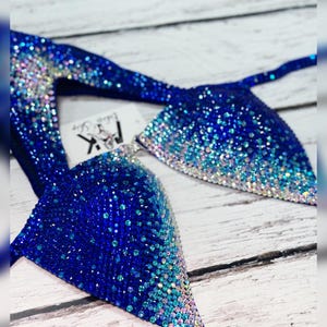 May include: A blue and white ombre bikini top with crystal embellishments. The top is made of a stretchy fabric and has a halter neck style.