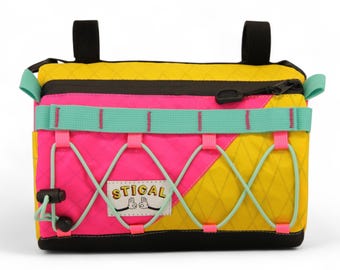Pode incluir: Bolsa de guiador de bicicleta colorida. A bolsa apresenta uma combinação de cores amarelo, rosa e turquesa, com detalhes em preto e fecho de correr. A palavra "STICAL" está impressa na frente.