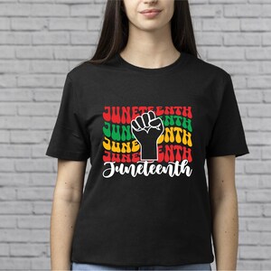 May include: Black t-shirt with a graphic design featuring the word "Juneteenth" in a colorful, retro font with a raised fist in the center.