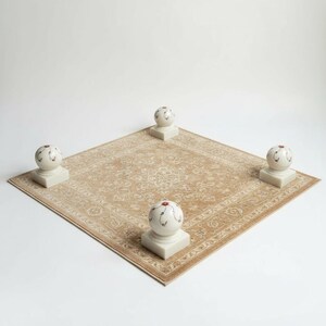 May include: A beige, patterned rug with four decorative, spherical objects. Each object is white with a red and black design. The rug is square and has a detailed, traditional design.