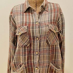 May include: A plaid button-down shirt in a mix of colors including red, black, white, and tan. The shirt has two chest pockets and two lower pockets. The shirt is displayed on a mannequin.
