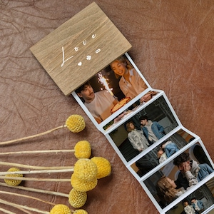 Könnte beinhalten: Ein Holzfotoalbum mit dem Wort "Love" auf dem Cover. Das Album ist geöffnet und zeigt eine Reihe von Fotos von Paaren in verschiedenen Umgebungen.