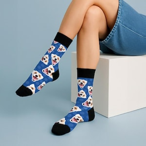 May include: Blue socks with a repeating pattern of smiling dog faces. The socks have black heels and toes, and a black band at the top. The dog faces are white and brown, with a happy expression.