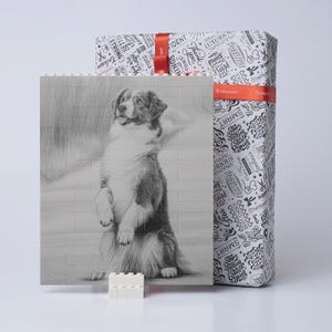 May include: A pencil sketch of a dog standing on its hind legs, set against a brick wall background. A wrapped gift box with a red ribbon is behind the sketch. The gift wrap has a black and white pattern with words.