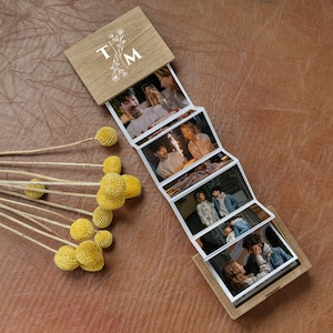 Könnte beinhalten: Ein Holzfotoalbum mit floralem Design und den Initialen "T.M." auf dem Cover. Das Album ist geöffnet und zeigt eine Reihe von Fotos eines Paares.