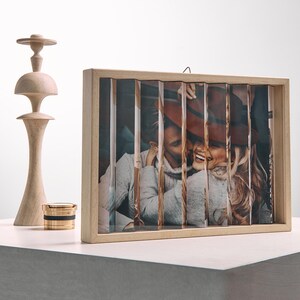 May include: A wooden photo frame with a picture of a couple, cut into vertical strips. The frame is light-colored, and the photo shows a man and woman smiling. A wooden decorative object and a gold and black container are also visible.