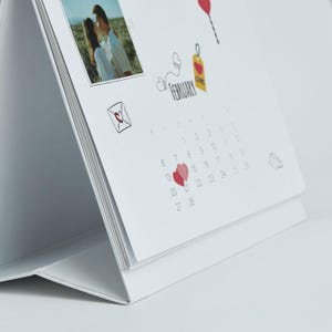 May include: A white desk calendar featuring a photo of a couple, with the month of February displayed. The calendar includes heart illustrations and the word "February". The calendar is designed to stand upright.