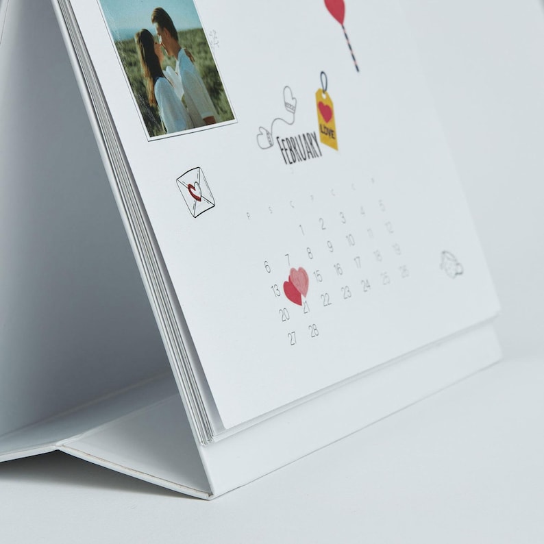 May include: A white desk calendar featuring a photo of a couple, with the month of February displayed. The calendar includes heart illustrations and the word "February". The calendar is designed to stand upright.