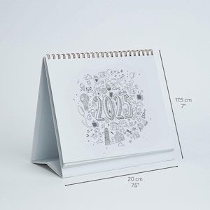 May include: A white desk calendar with a spiral binding, featuring a doodle design and the year 2025. The calendar is 7 inches tall and 7.5 inches wide.