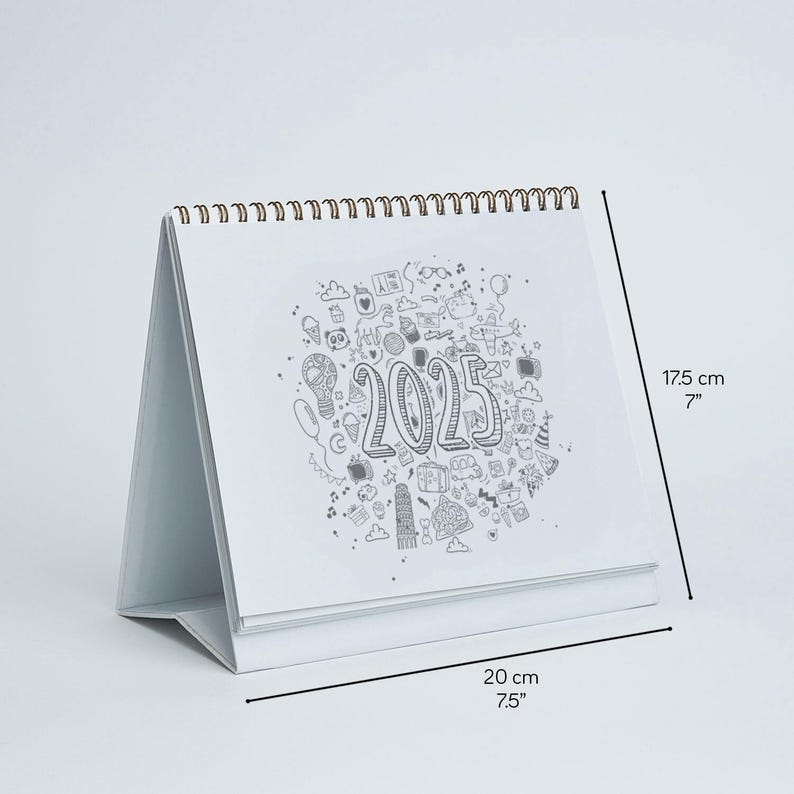 May include: A white desk calendar with a spiral binding, featuring a doodle design and the year 2025. The calendar is 7 inches tall and 7.5 inches wide.