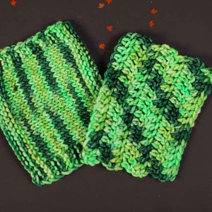 May include: Two green and black striped knitted dishcloths. The dishcloths are made of a soft, textured yarn.