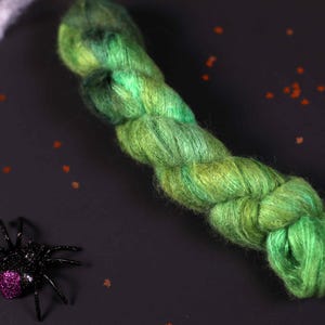 May include: A skein of green and blue yarn with a fuzzy texture. The yarn is twisted and knotted, creating a unique and interesting pattern.