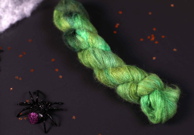 May include: A skein of green and blue yarn with a fuzzy texture. The yarn is twisted and knotted, creating a unique and interesting pattern.