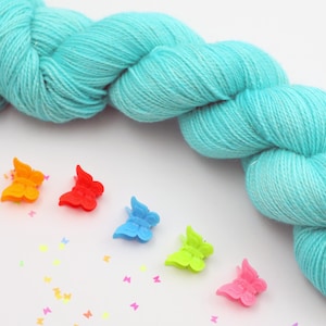 May include: A skein of light blue yarn with a rainbow of plastic butterfly clips scattered around it.