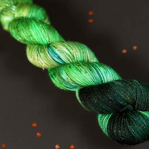 May include: A skein of green and blue yarn with gold glitter. The yarn is wound into a loose coil.