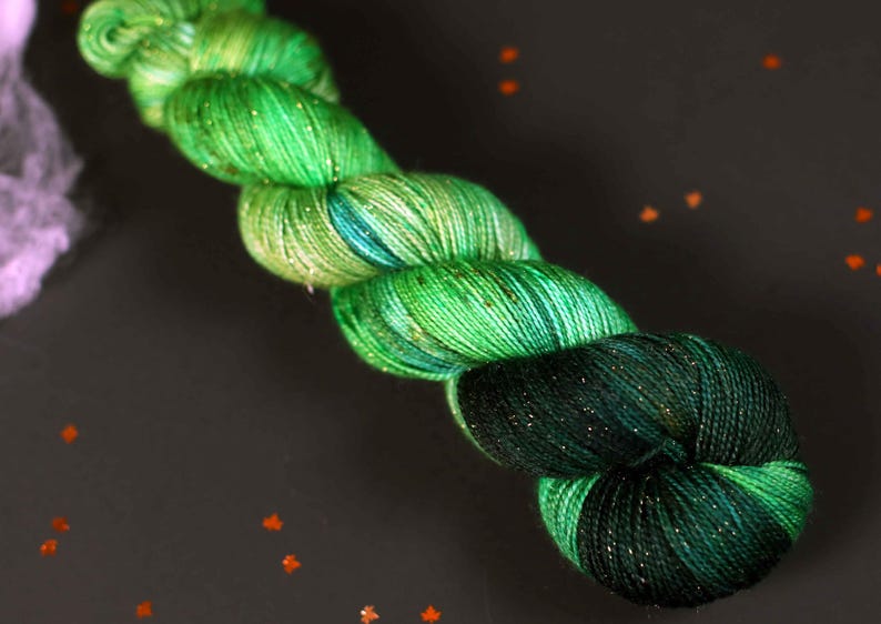 May include: A skein of green and blue yarn with gold glitter. The yarn is wound into a loose coil.