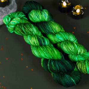 May include: Two skeins of green and black yarn with a variegated colour pattern. The yarn is soft and fluffy, and it would be perfect for knitting or crocheting.